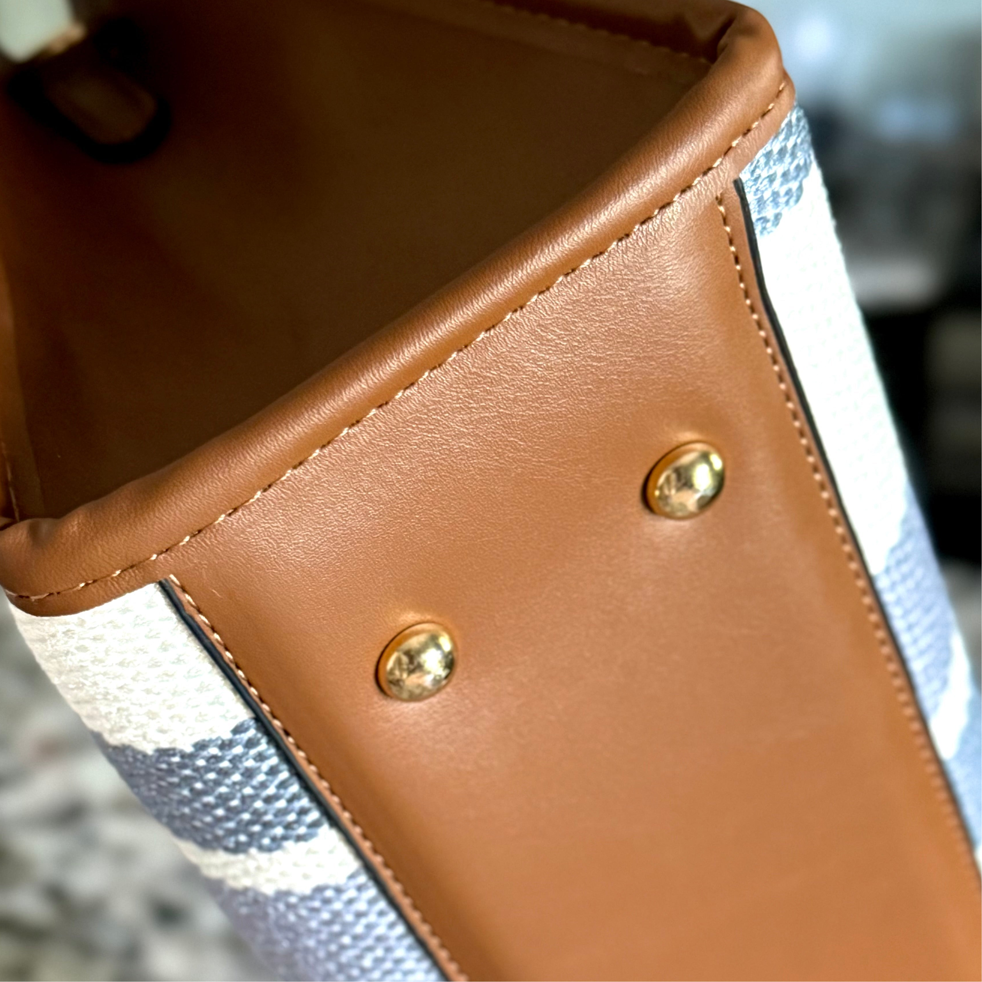 Close-up of a brown leather and fabric handbag with gold studs.