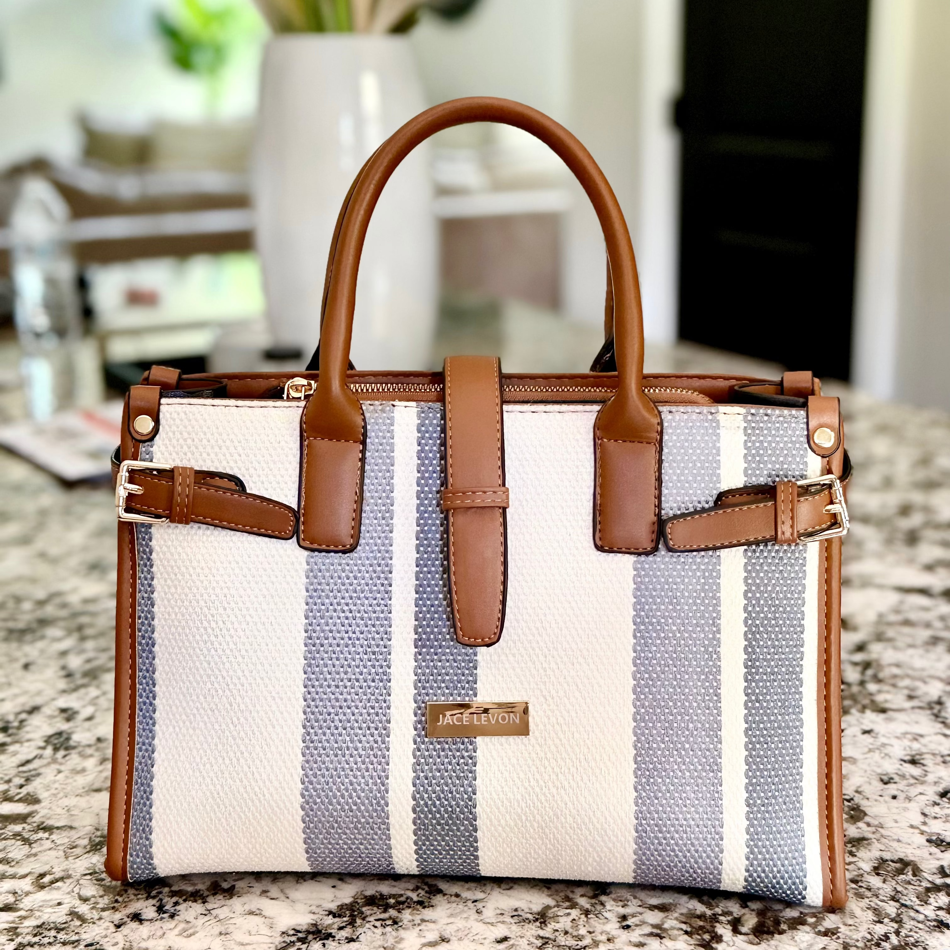 Striped handbag with brown handles and trim on a marble surface